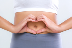 Woman creating a shape of a heart with her hands in front of her bare tummy